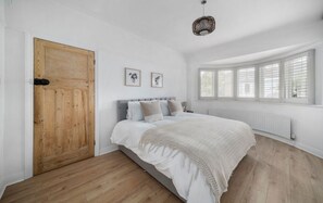 Ein Schlafzimmer mit Holztür, einem Bett mit weißer Bettwäsche, einem Heizkörper und einem Fenster mit Rollläden.