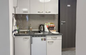 A compact kitchenette with a sink, a kettle, a coffee maker, and a dish rack.