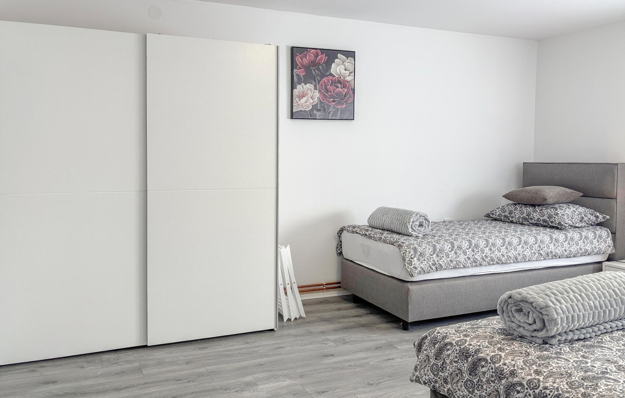 A modern bedroom with a grey sofa bed, a grey headboard, and a white wardrobe.