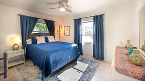 A bedroom with a bed, a nightstand, a lamp, a ceiling fan, and a window with curtains. - Charming Remodeled Cottage | Walk to Park Ave (Winter Park)