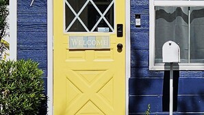 A yellow door with a welcome sign, a mailbox, and the number 617 on a blue house. - Charming Remodeled Cottage | Walk to Park Ave (Winter Park)