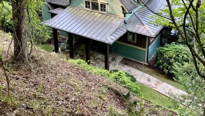 Una casa rústica con fachada verde, un porche cubierto y un camino de piedra que conduce a la entrada.