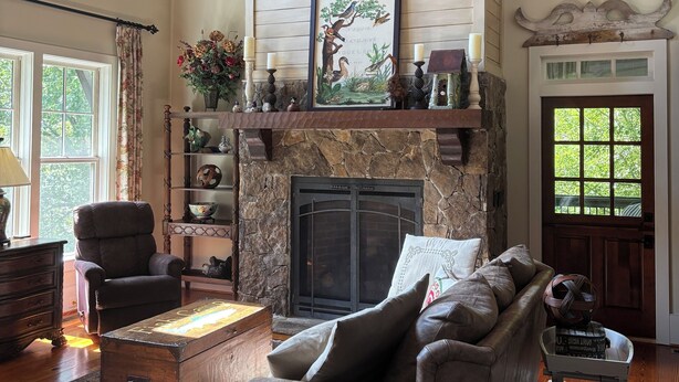 Una sala de estar acogedora con chimenea, un sofá confortable, techo de madera y un revestimiento de piedra alrededor de la chimenea.