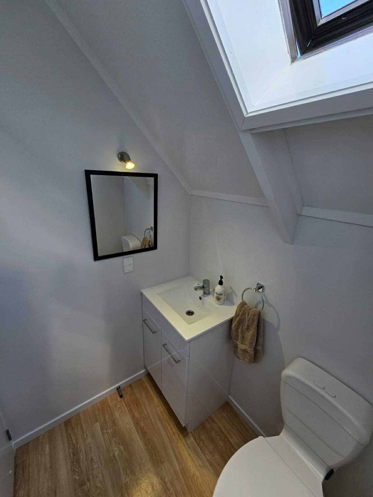 A modern bathroom with a skylight, a white sink, a toilet, and a mirror.