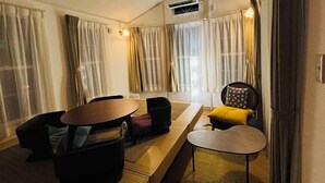 A hotel room with a sofa, a small table, a chair, and a window with curtains. - Inn the Fuji (Fujiyoshida)