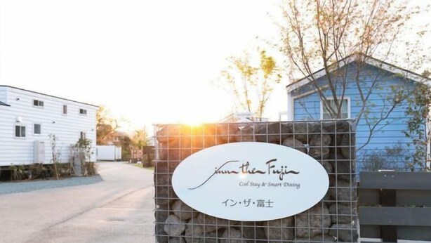 A sign for 'Inn the Fuji' with a stone wall and a blue building in the background. - Inn the Fuji (Fujiyoshida)