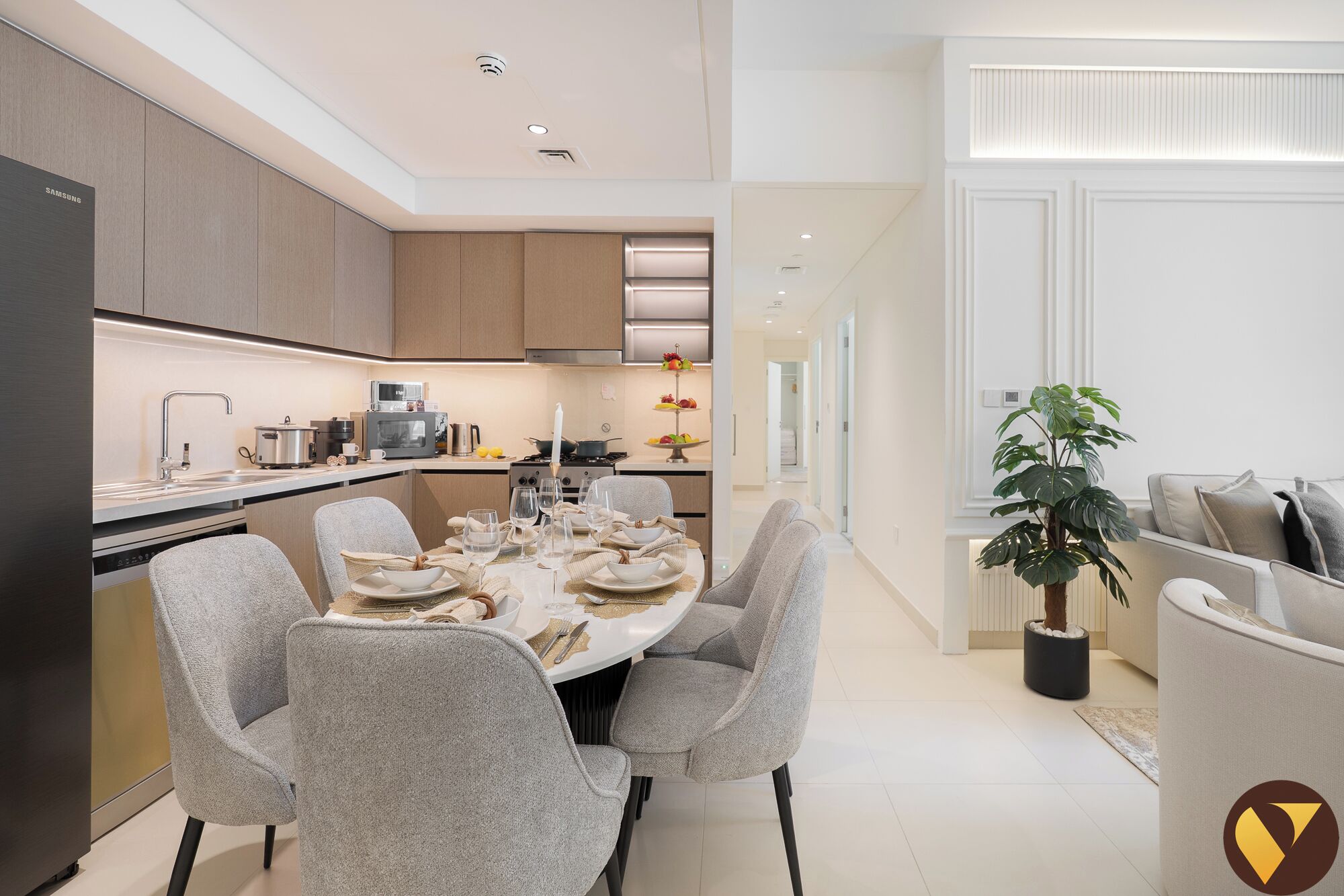 A modern kitchen with built-in appliances, a dining area with a round table and grey chairs, and a potted plant in the corner.
