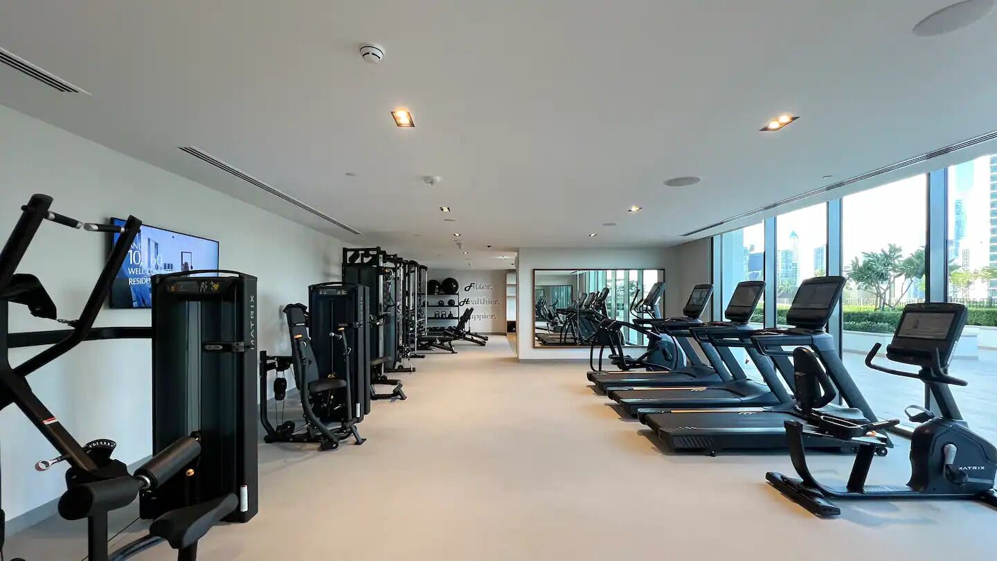 Et moderne fitnesscenter med forskellig træningsudstyr, store vinduer og en ren, rummelig indretning.