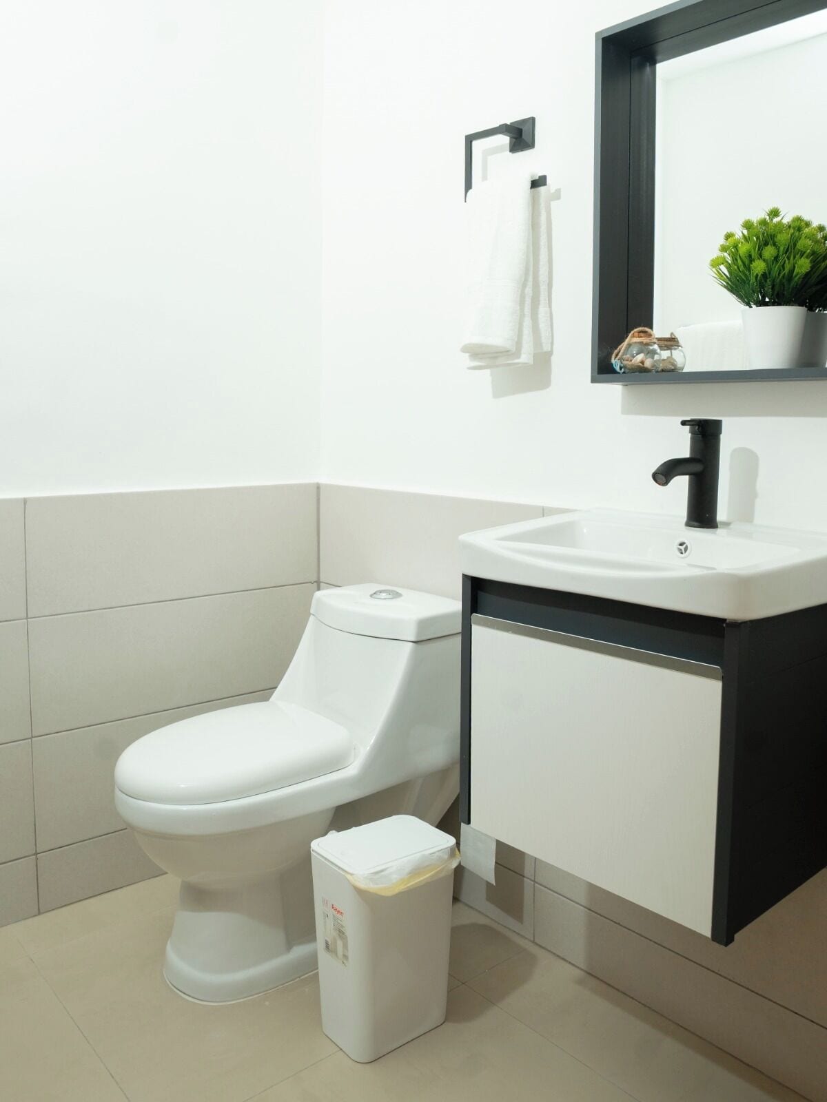 Une salle de bain moderne avec des toilettes blanches, un lavabo noir et une poubelle blanche.