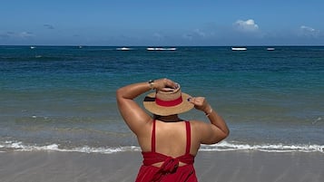 A person in a red dress walking on a sandy beach with the ocean in the background.
