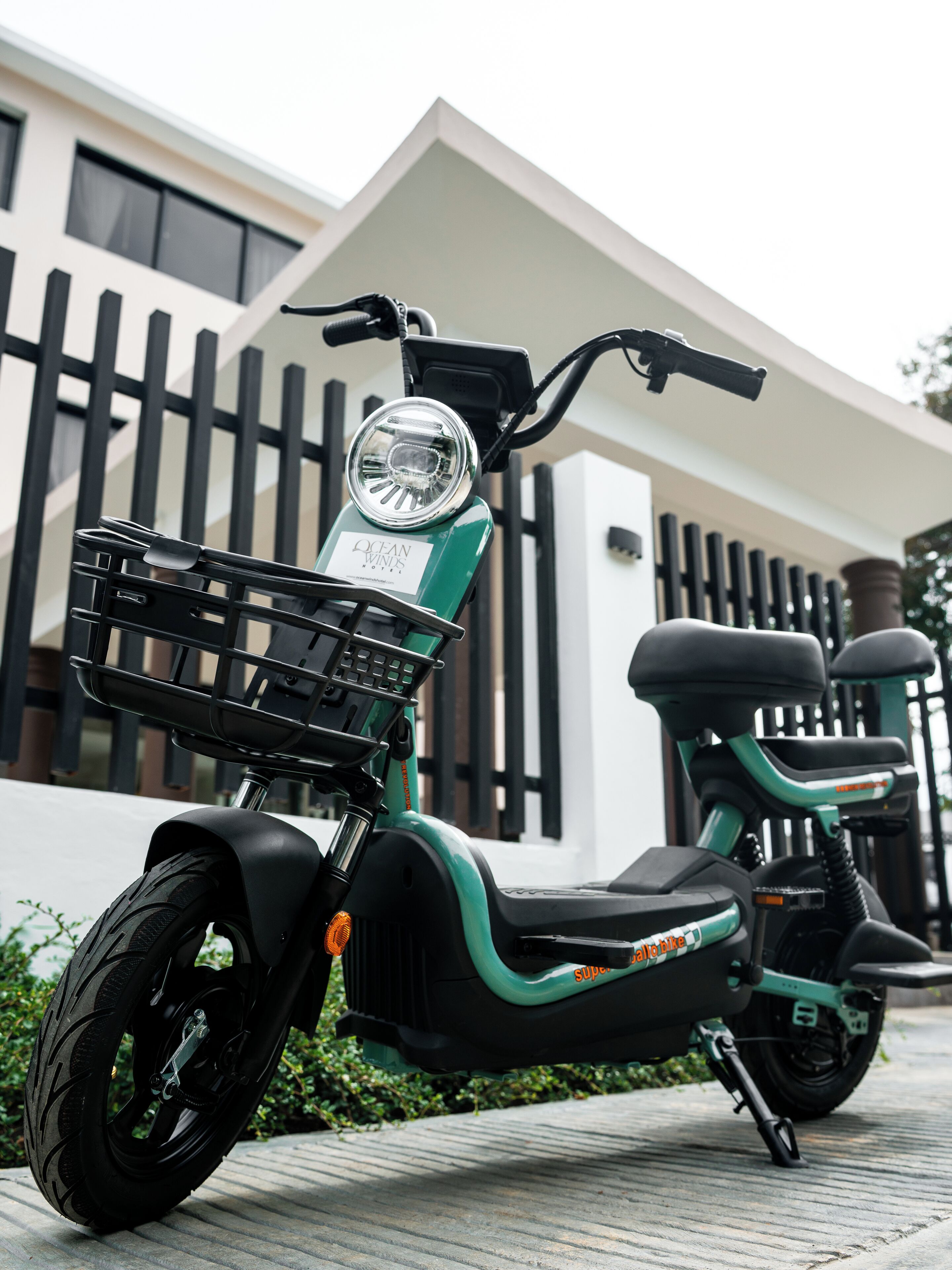 Une trottinette électrique verte est garée devant un bâtiment moderne à la façade blanche et aux éléments décoratifs noirs.