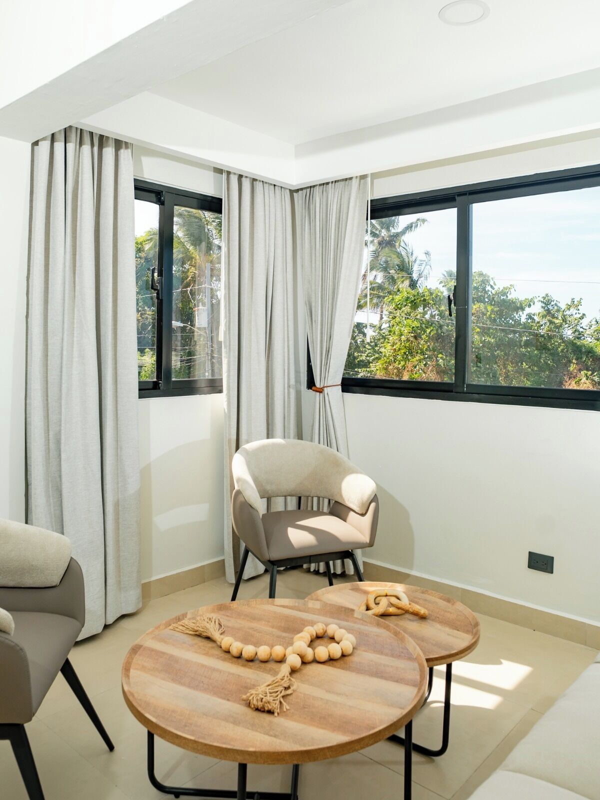 A modern room with a large window, a beige armchair, a round wooden table, and a sofa.
