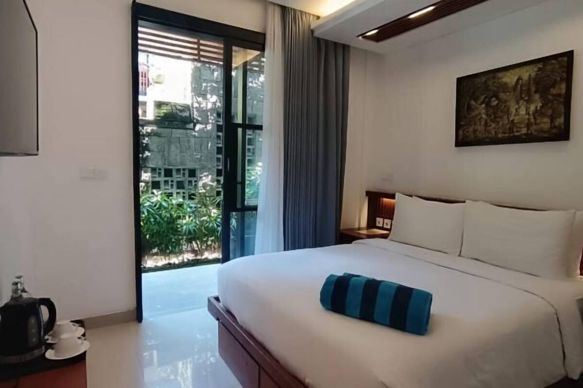 A hotel room with a bed, a painting on the wall, and a view through a glass door.