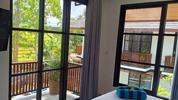 A room with large windows, a bed, a blue striped cushion, and a view of a wooden deck and greenery outside. - Paripadi Studio Canggu (Bali)