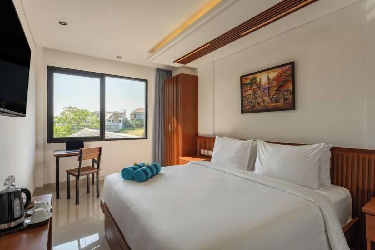 A hotel room with a large bed, a desk, a chair, a painting on the wall, and a view of the outside.