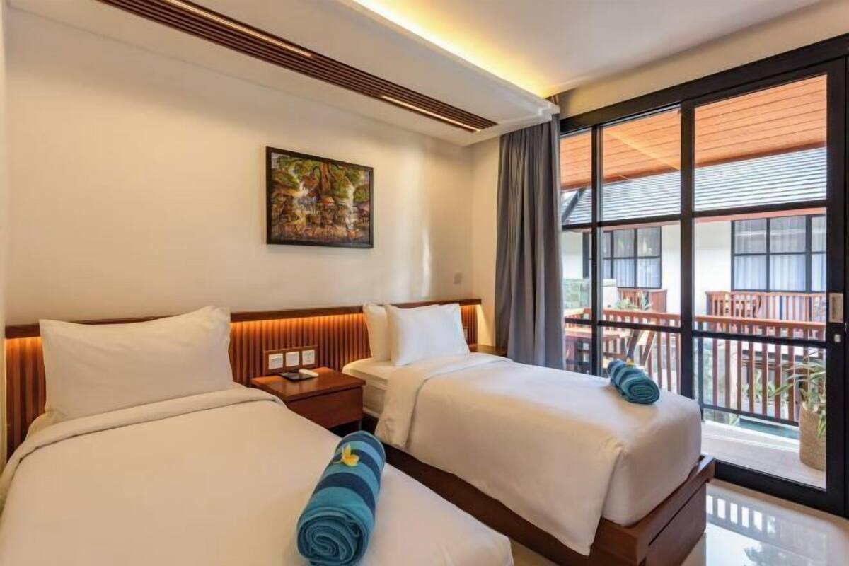 A hotel room with two beds, a painting on the wall, and a balcony with wooden furniture.