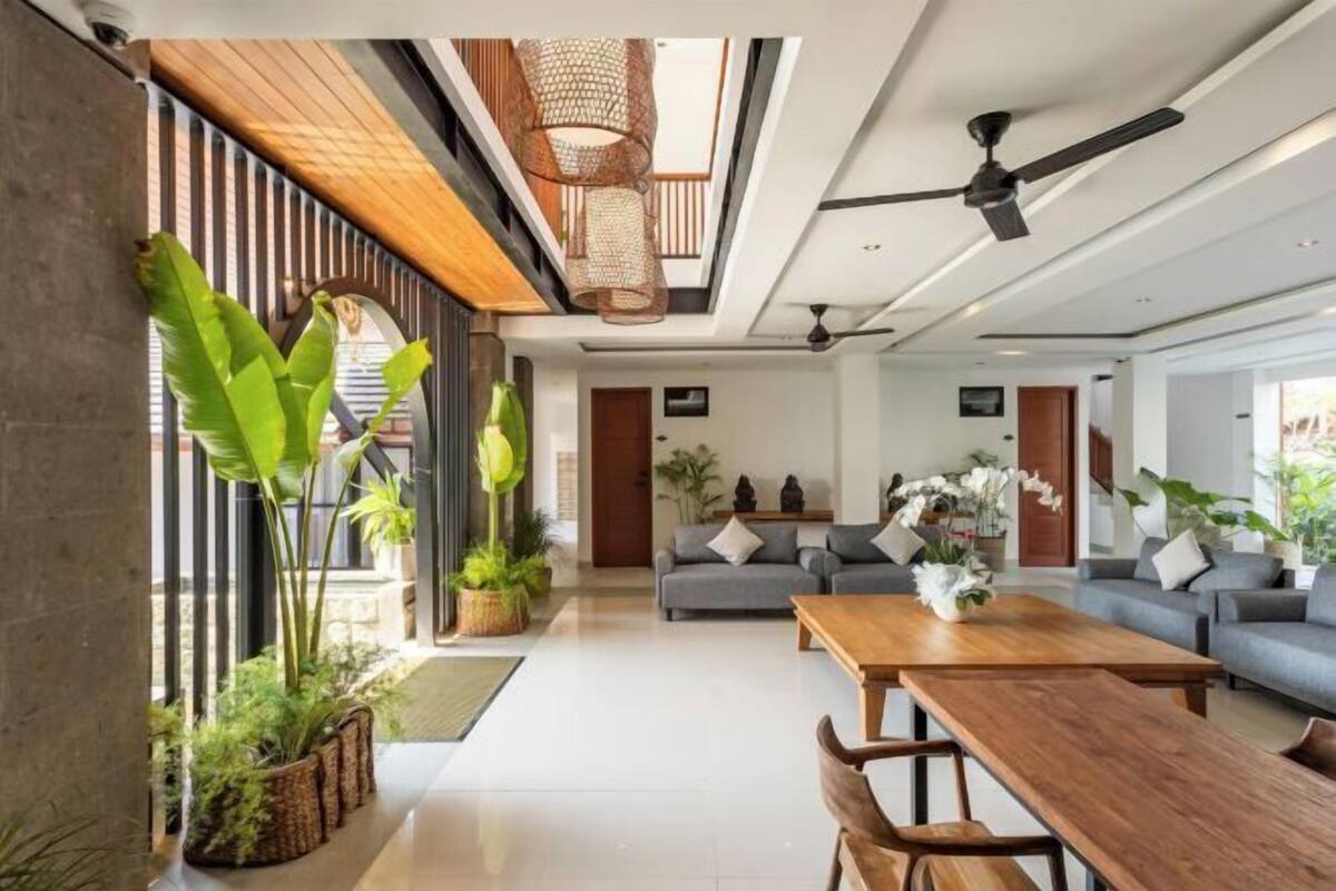 A modern living room with a sofa set, a wooden dining table, and potted plants.