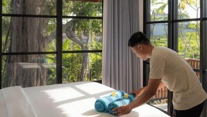 A person folding towels on a bed with a view of trees and a wooden deck outside. - Paripadi Studio Canggu (Bali)