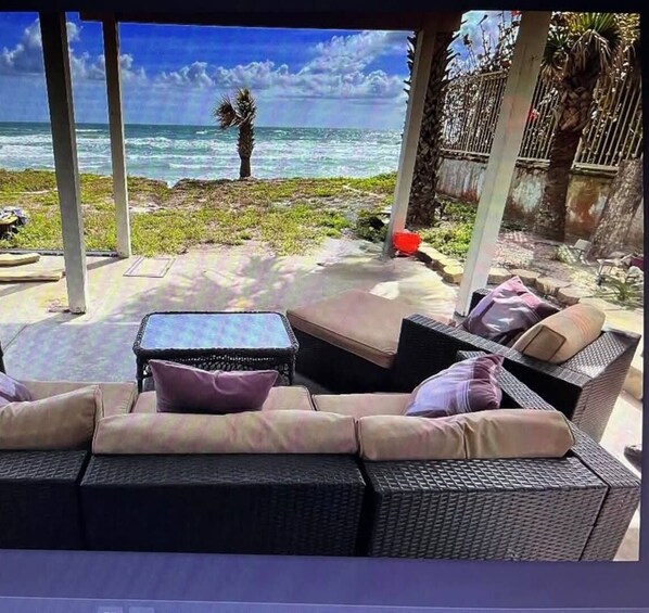 Zona relax all'aperto coperta, con mobili in vimini e cuscini, con vista sull'oceano.