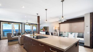 A modern kitchen with a large island, pendant lighting, and a view of the ocean. - Luxury Oceanfront Panoramic Views, Private Sauna & Beach Access - Vrkcv (Kailua-Kona)