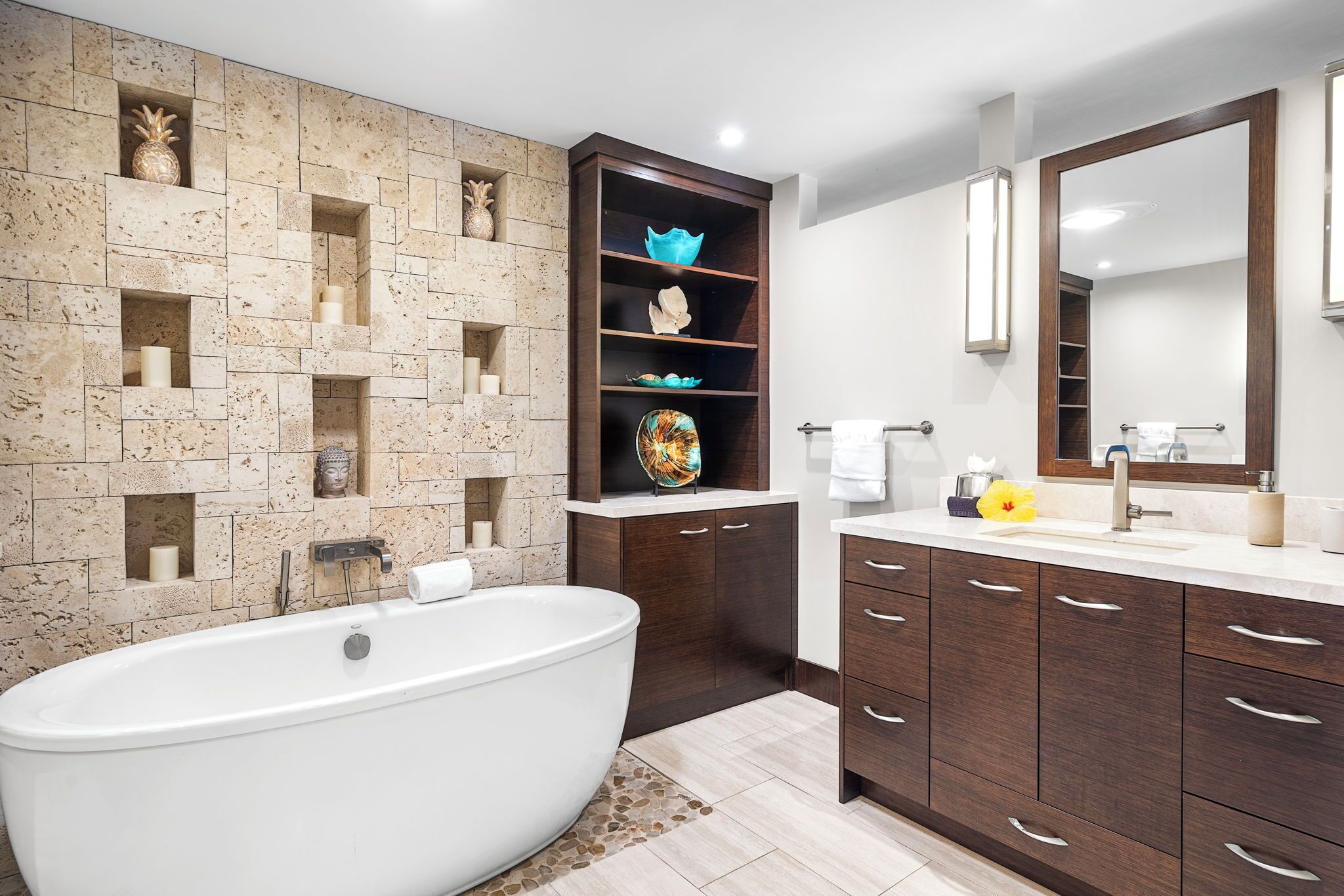 A modern bathroom with a freestanding bathtub, built-in shelves with decorative items, a large mirror, and dark wooden cabinets.