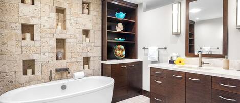 A modern bathroom with a freestanding bathtub, built-in shelves with decorative items, a large mirror, and dark wooden cabinets.