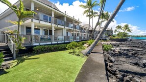 A two-story beachfront property with a balcony, palm trees, and a well-maintained lawn. - Luxury Oceanfront Panoramic Views, Private Sauna & Beach Access - Vrkcv (Kailua-Kona)