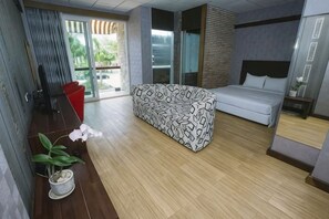 Una habitación de hotel moderna con un sofá, una cama, una mesita, una planta en maceta y un ventanal corredero que da a un espacio exterior.