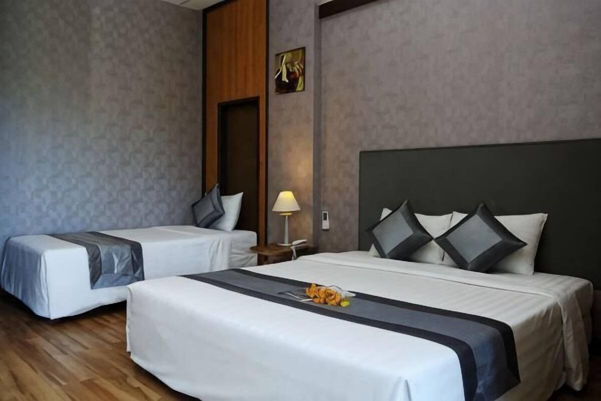 A hotel room with two beds, a wooden headboard, a nightstand with a lamp, and a painting on the wall.