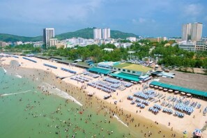 Un complexe hôtelier de bord de mer doté de nombreuses chaises longues, de parasols et d’un grand bâtiment surmonté d’un toit végétalisé.