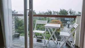 Ein Balkon mit Tisch und zwei Stühlen, einer Glastür und Blick auf Grünflächen sowie ein geparktes Auto.