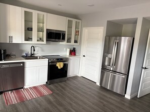 A modern kitchen with white cabinets, stainless steel appliances, a dishwasher, and a red striped rug. - Welcoming 2-bed/1ba walk-out basement in Castle Pines (Castle Pines)