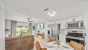 Une cuisine moderne avec des meubles blancs, un réfrigérateur en acier inoxydable, un four à micro-ondes et un four traditionnel. On y trouve une table à manger avec des chaises et une plante en pot.
