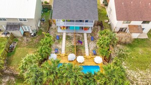 Un jardin à l’arrière d’une maison, avec une terrasse en bois, une piscine et un espace clos doté d’équipements de jeux colorés.