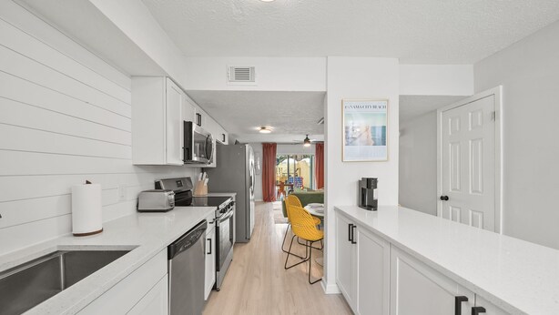 Une cuisine moderne avec des meubles blancs, un évier en acier inoxydable et un coin repas agrémenté d’une chaise jaune.