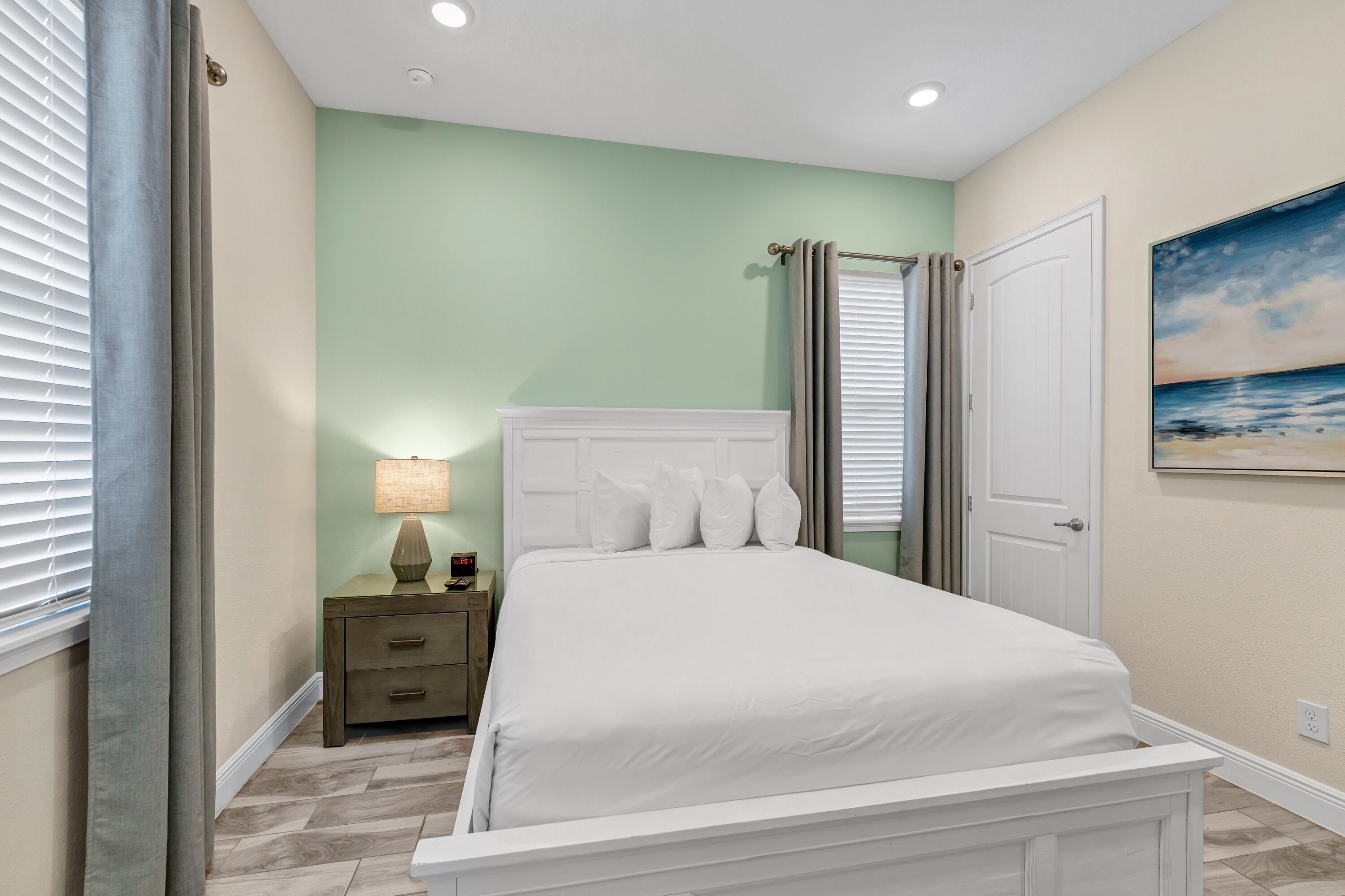 A bedroom with a white bed, a nightstand with a lamp, and a painting on the wall.