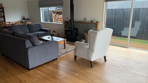 Un salon avec un canapé gris, un fauteuil blanc, une table basse en bois et un poêle à bois noir.