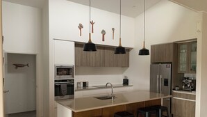 Une cuisine moderne dotée d’un îlot central, de tabourets de bar, d’un four encastré, d’un réfrigérateur et de luminaires suspendus.