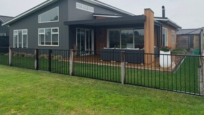 Une maison moderne à deux étages, dotée d’un patio couvert, de grandes fenêtres et d’une cour clôturée.