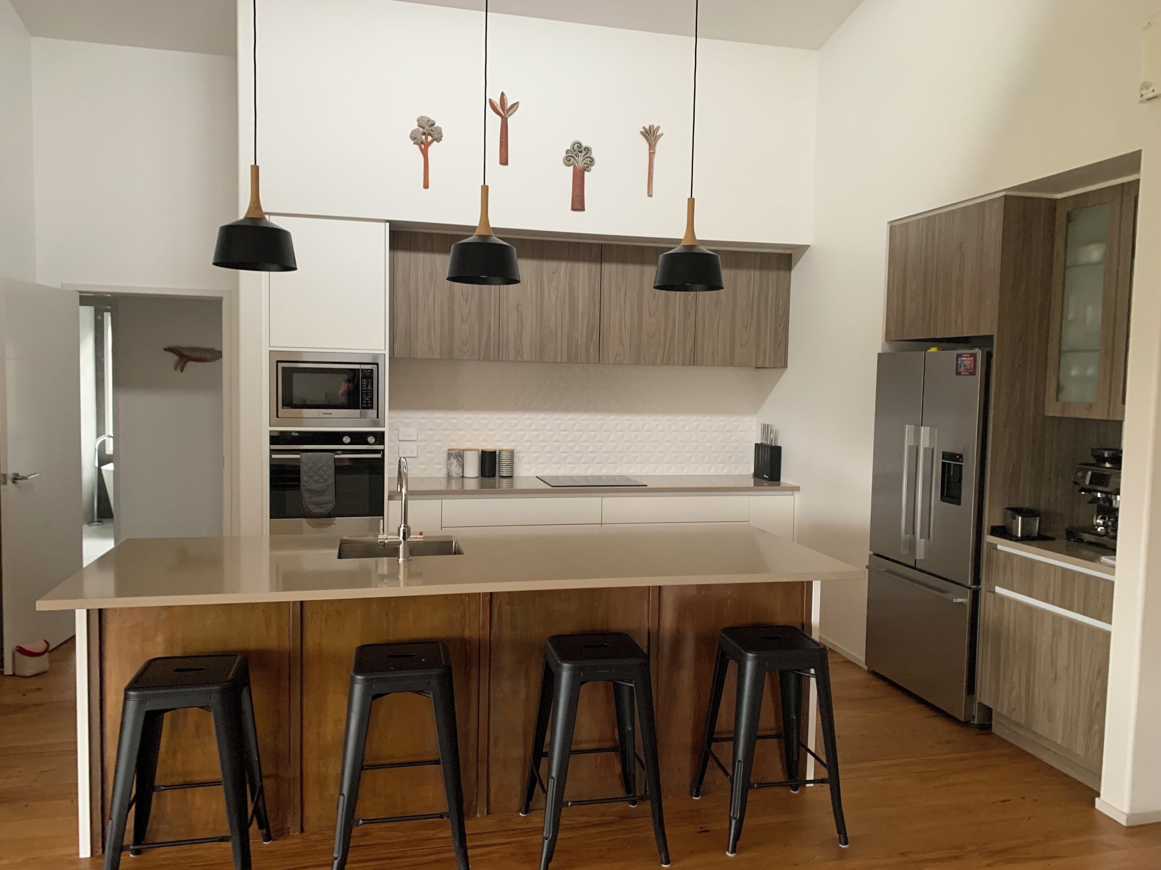 Une cuisine moderne dotée d’un grand îlot central, de meubles en bois, d’appareils électroménagers en acier inoxydable et de tabourets de bar noirs.