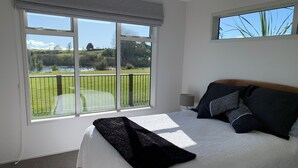 Une chambre avec un grand lit, une table de chevet et une vue sur un terrain de golf, visible par la fenêtre.