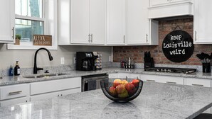 Una cocina moderna con armarios blancos, encimera de granito, cafetera y frutero.