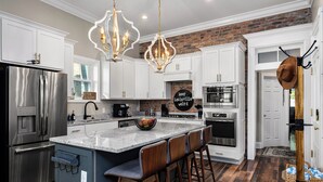 Una cocina moderna con armarios blancos, un refrigerador de acero inoxidable, una encimera de granito y una pared decorativa de ladrillo.
