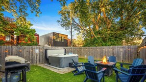 Un patio trasero con jacuzzi, un pozo de fuego y sillas Adirondack.