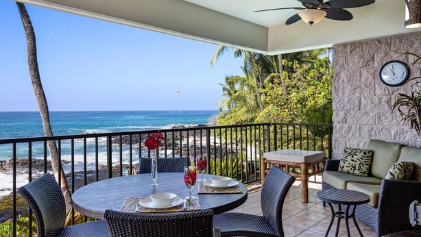 A balcony with a table set for two, overlooking a beach and ocean. - Direct Ocean Front Steps From the Beach Large Lanai - Vrkcv (Kailua-Kona)