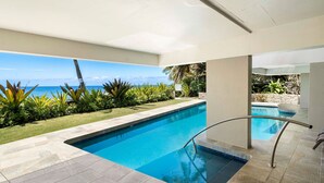 A swimming pool with a clear view of the ocean, surrounded by a well-maintained lawn and tropical plants. - Direct Ocean Front Steps From the Beach Large Lanai - Vrkcv (Kailua-Kona)