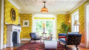 A room with a fireplace, a large window, and a patterned rug. - The Waldoboro Inn Room 5 (Waldoboro)