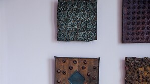 A chair with a woven seat and dark wooden frame, a glass table with a potted plant and books, and three decorative wall hangings. - The Waldoboro Inn Room 5 (Waldoboro)