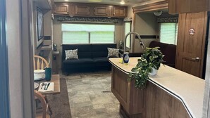 Une cuisine compacte pour camping-car, comprenant un coin repas, un évier et une fenêtre avec stores.
