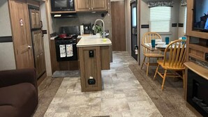 Une cuisine compacte pour camping-car, dotée d’un îlot central, de meubles en bois et d’un coin repas avec des chaises.